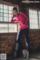 A woman in a pink shirt and blue leggings leaning against a brick wall.