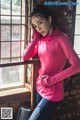 A woman in a pink hoodie leaning against a window.