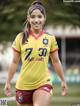 A woman in a yellow shirt and red shorts on a soccer field.